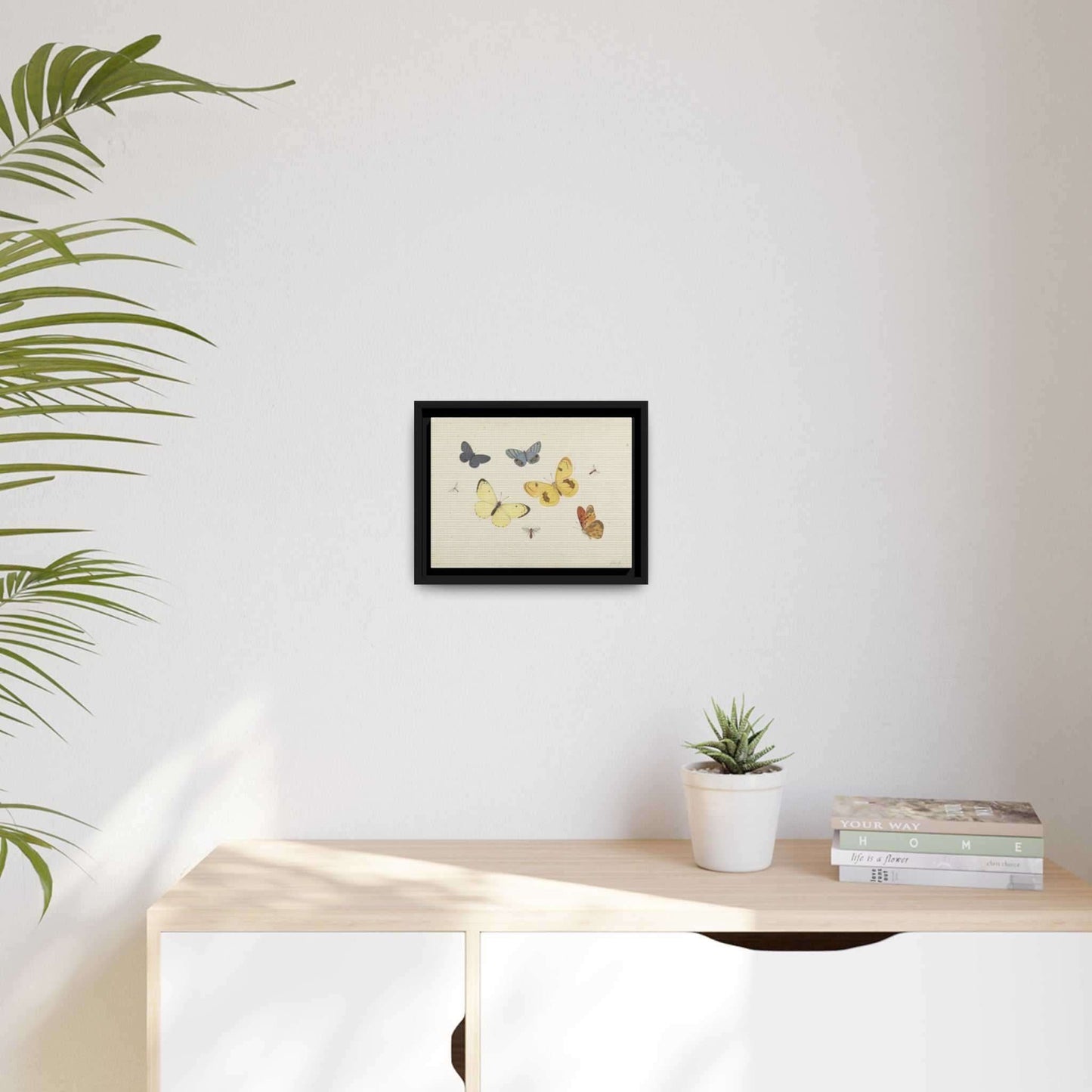 Black wooden framed 'Butterflies' canvas art print - yellow blue and orange butterflies painted in a botanical illustration style - 9 x 12 inches ready to hang sustainable wood print. pictured above a white dresser a plant is on the left side