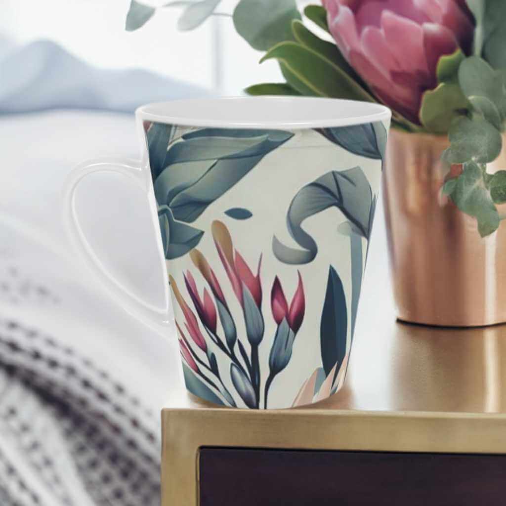 'Bohemian Garden' Latte Mug, 12oz scratch resistant white ceramic. Sage green and burgundy botanical print. Perfect cup for enjoying your favorite drink in style. Pictured on a bedroom side table with a vase of pink protea flowers beside it. a bed with white bedding and duvet cover in the background c shaped handle 12oz - scratch resistant 'Bohemian Garden' Latte Mug, 12oz - Free Shipping in canada