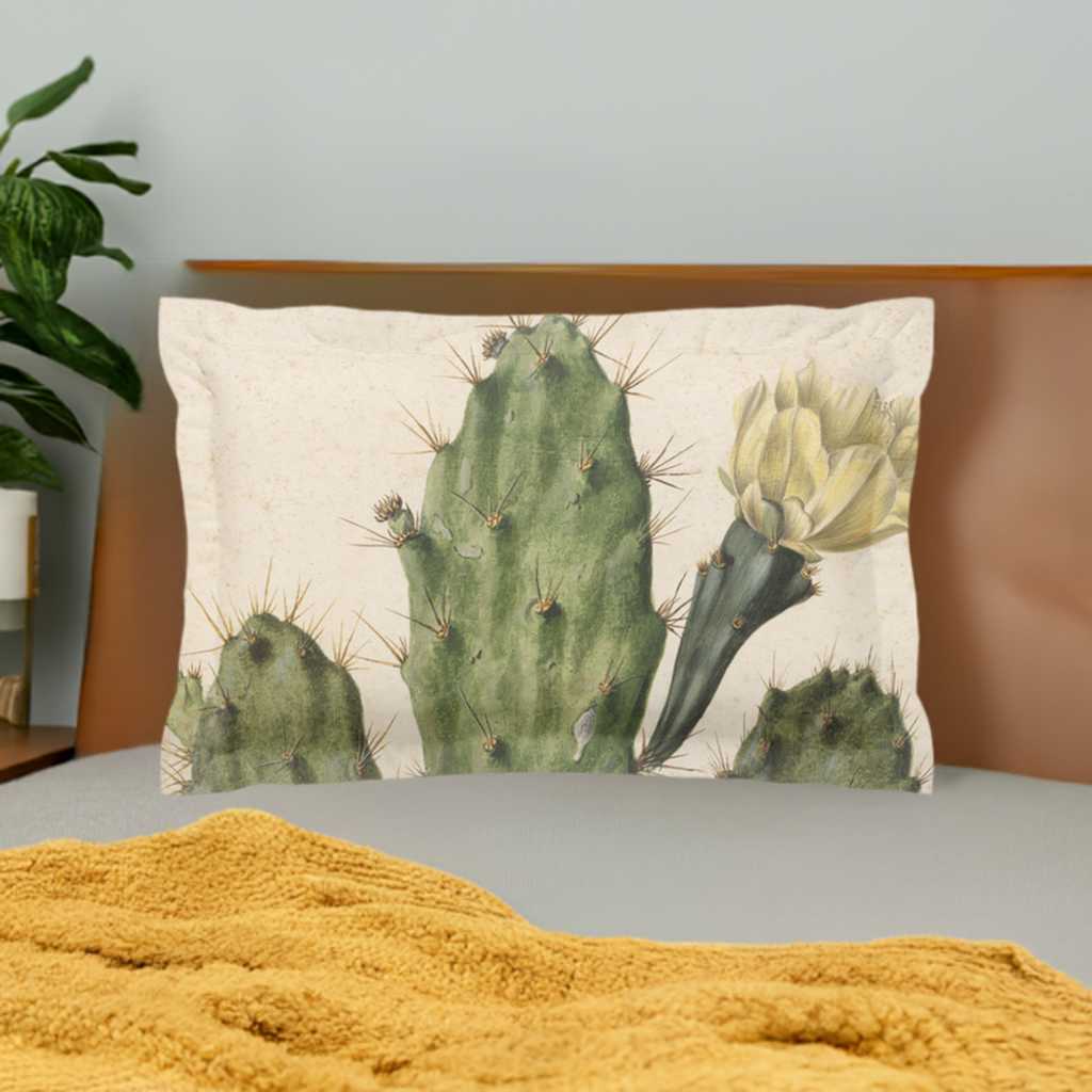 Pillow sham with 2 inch flange - micro fibre - Cactus with yellow flower on cream background - Pictured in front of a wooden headboard on a white duvet cover behind a yellow knit blanket lying on the bed a plant sits on a beside table on the left side